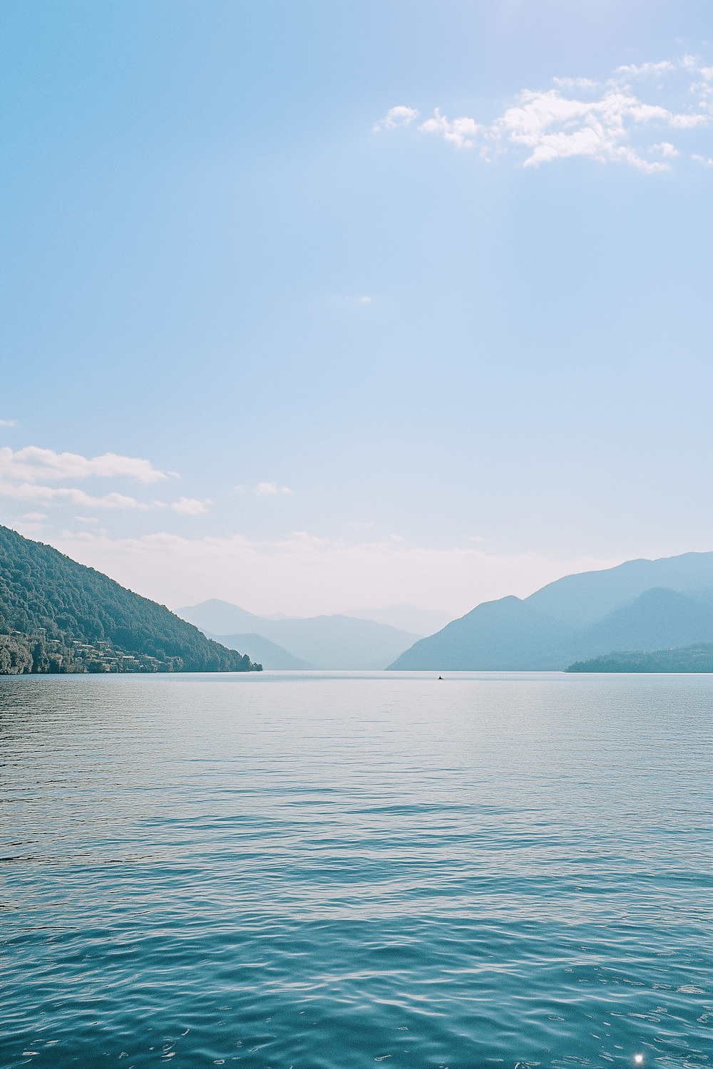 A wide lake ringed by green hills under a clear sky